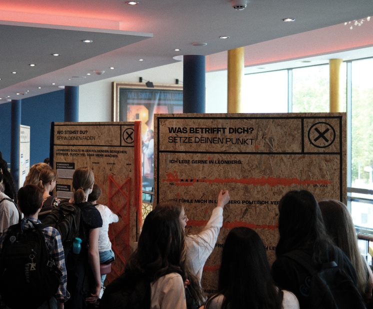 Students standing in front of a exhibition wall spinning a yarn between nails in the wood