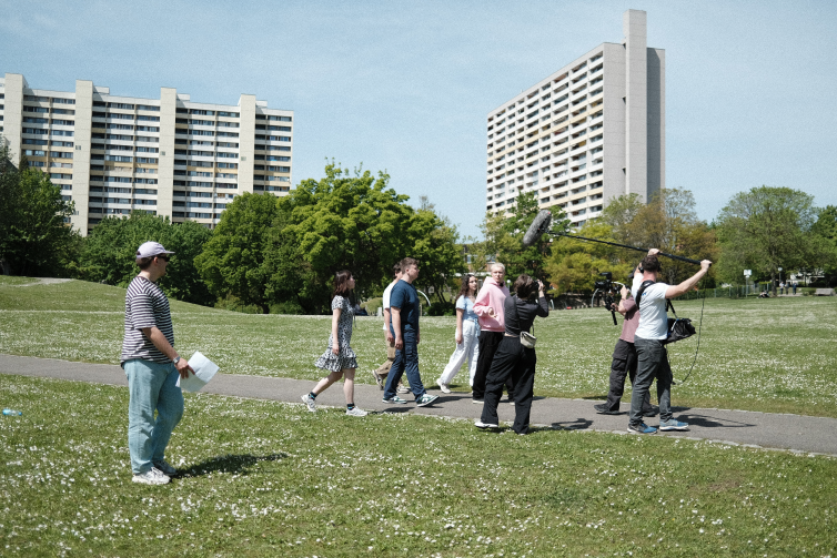 Making of scene showing a group of young people walking through a park, being filmed by camera man