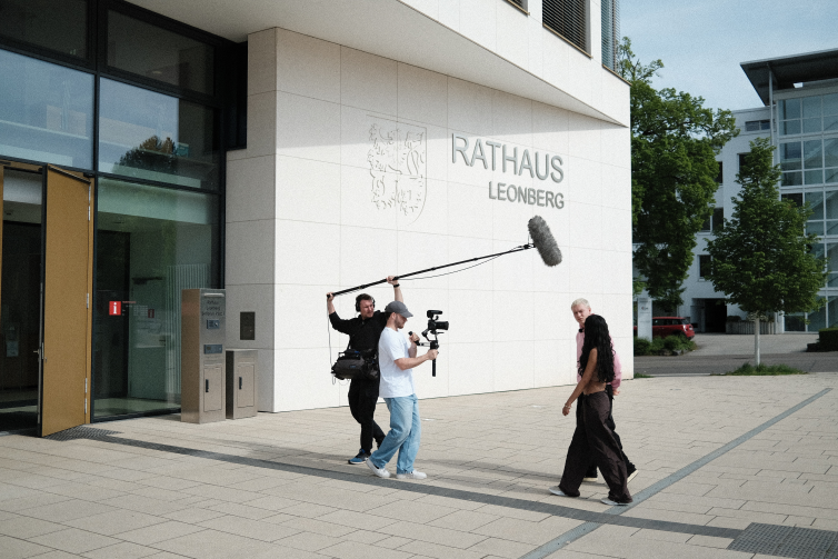 Making of scene showing a camera man and sound man walking infront of two young actors in front of the Townhall Leonberg